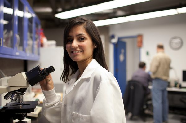 Female in lab coat smiling with a microscope
