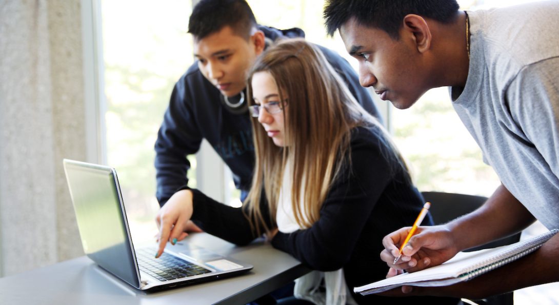 Image of students on campus surrounding a laptop