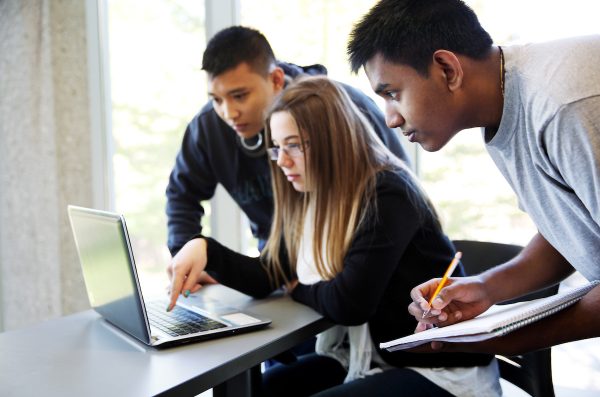 three students surrounding a laptop