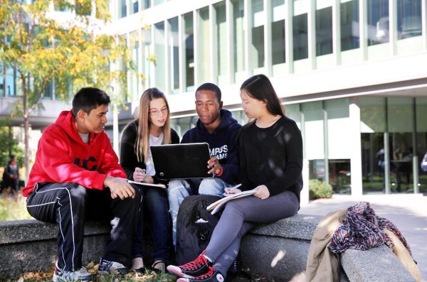 Four students sitting outside looking at a laptop