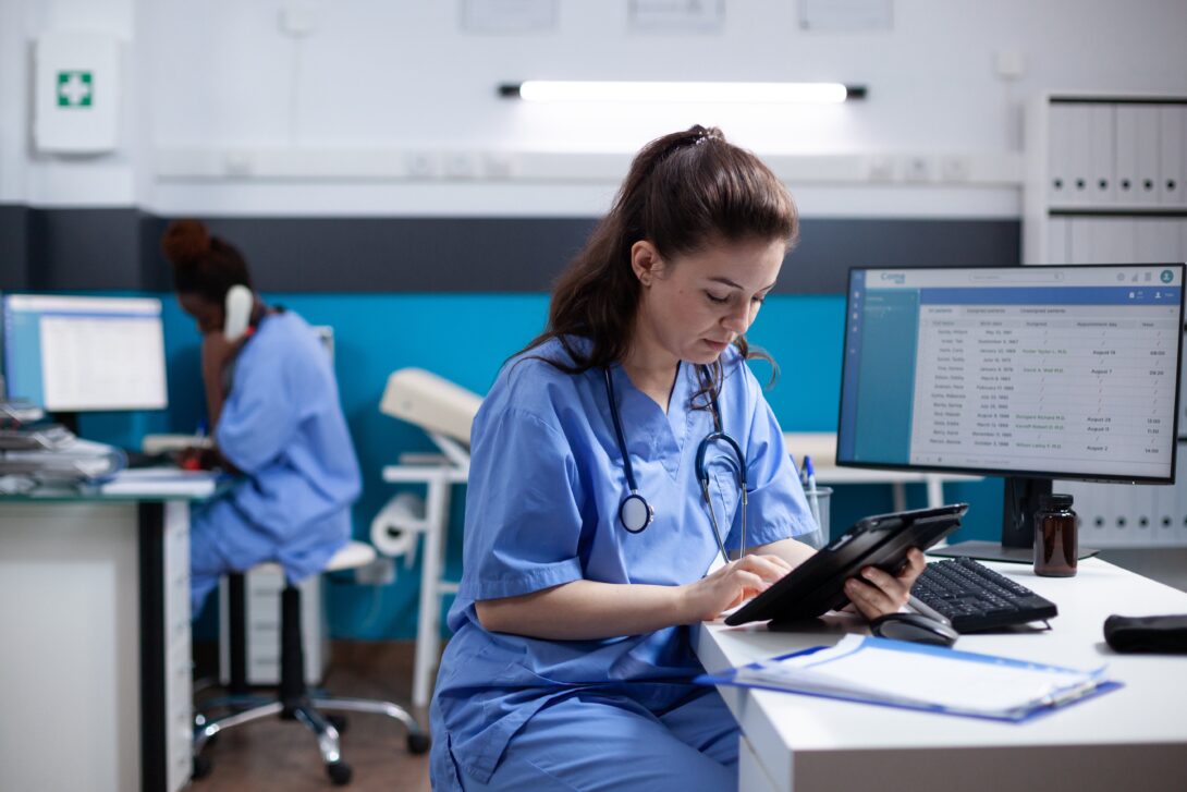 Nurse sitting at desk looking at tablet